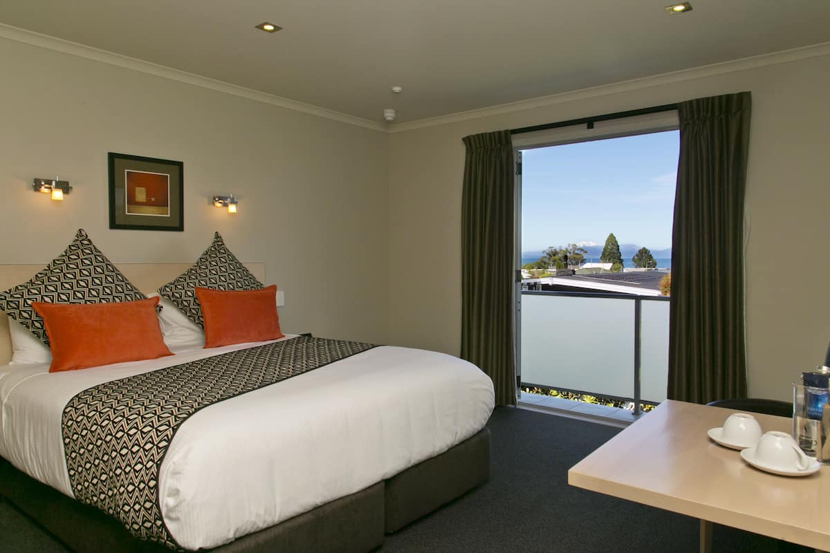 A hotel room with a large bed, a balcony with a view, and a table with cups and a water bottle.
