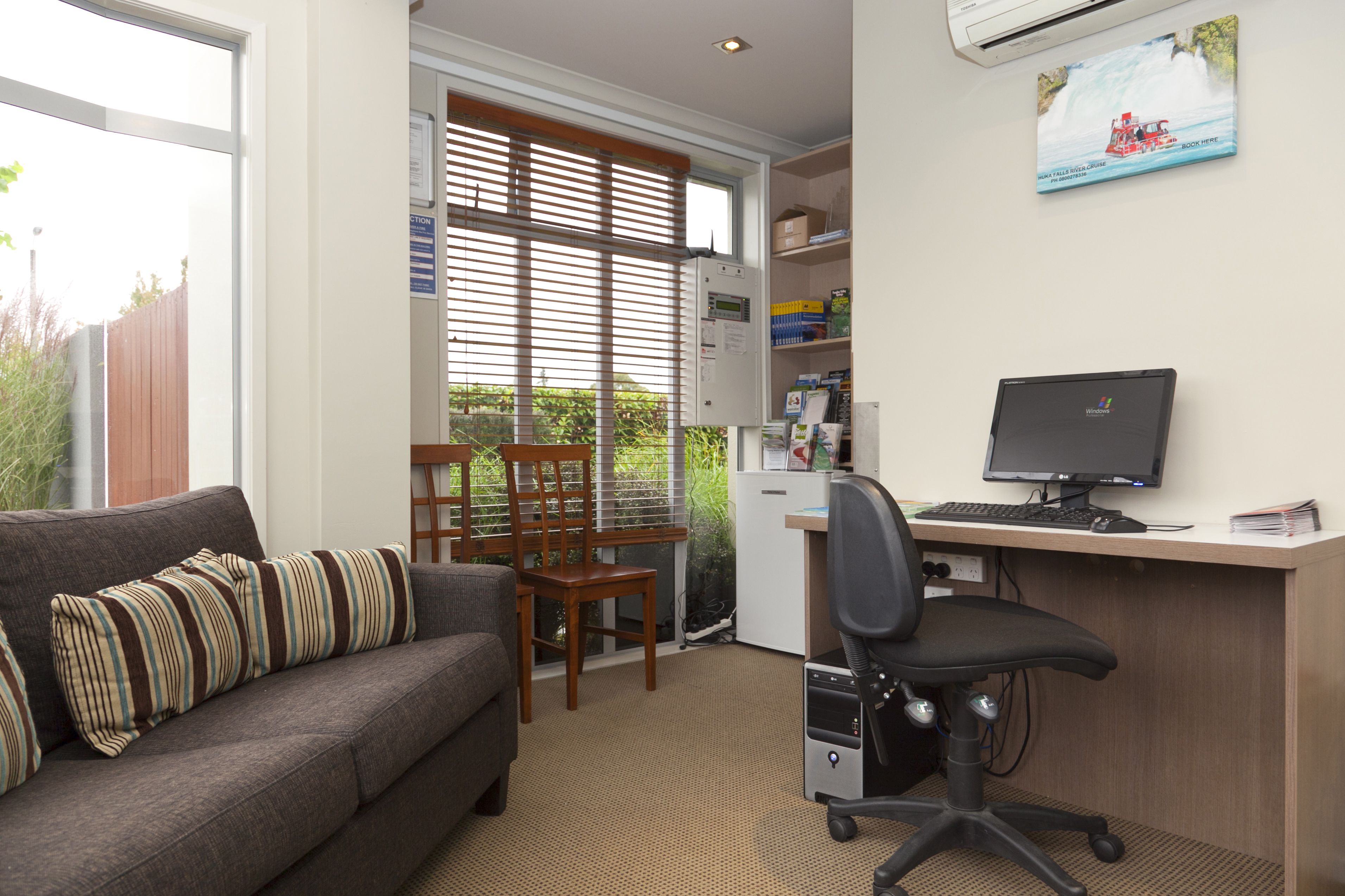 A room with a sofa, a desk with a computer, a chair, and a window with blinds.