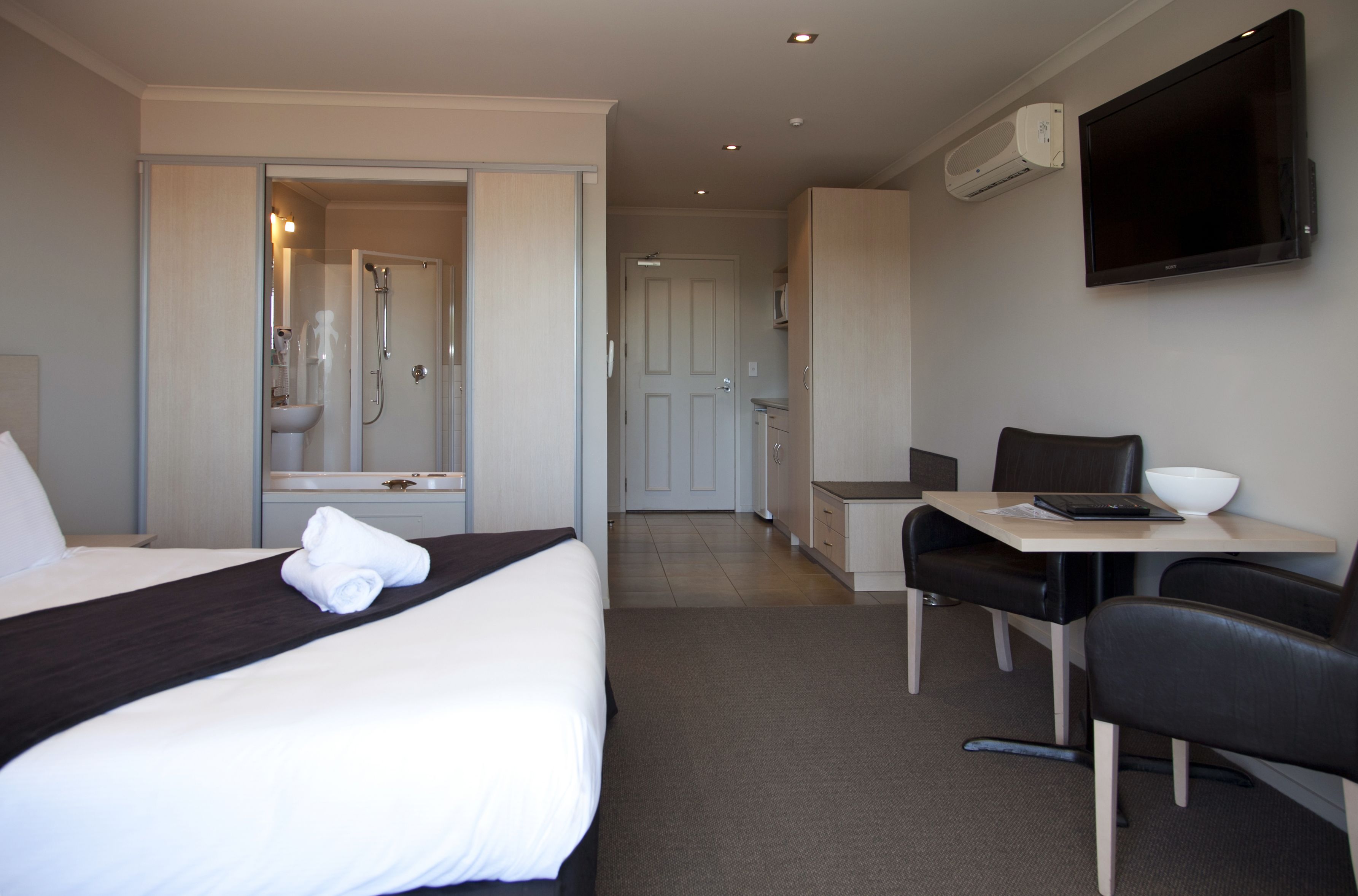 Habitación de hotel con cama, escritorio, silla, televisor y baño con ducha y lavamanos.