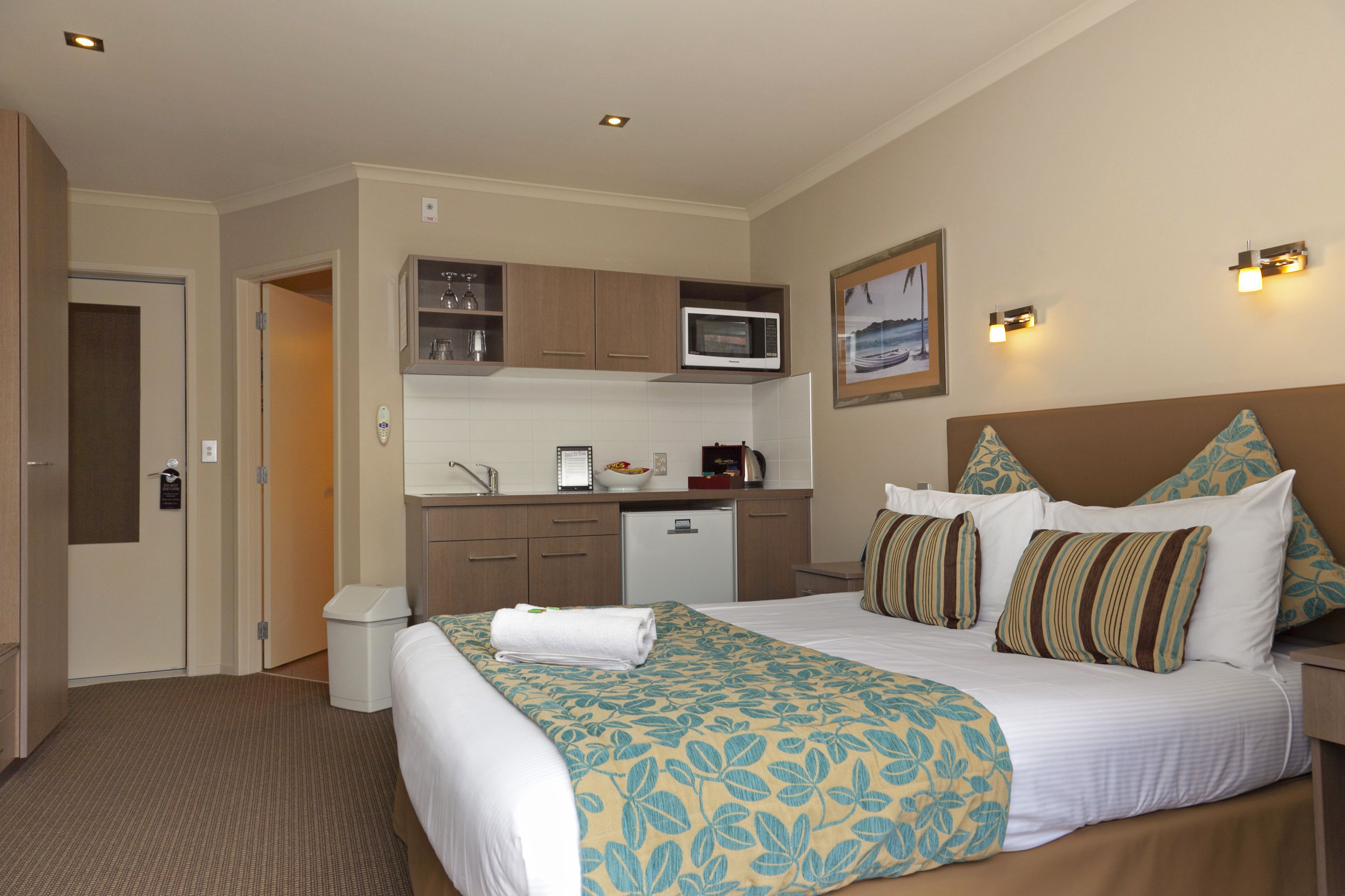 A hotel room with a bed, a desk, a microwave, a sink, and a small kitchenette.