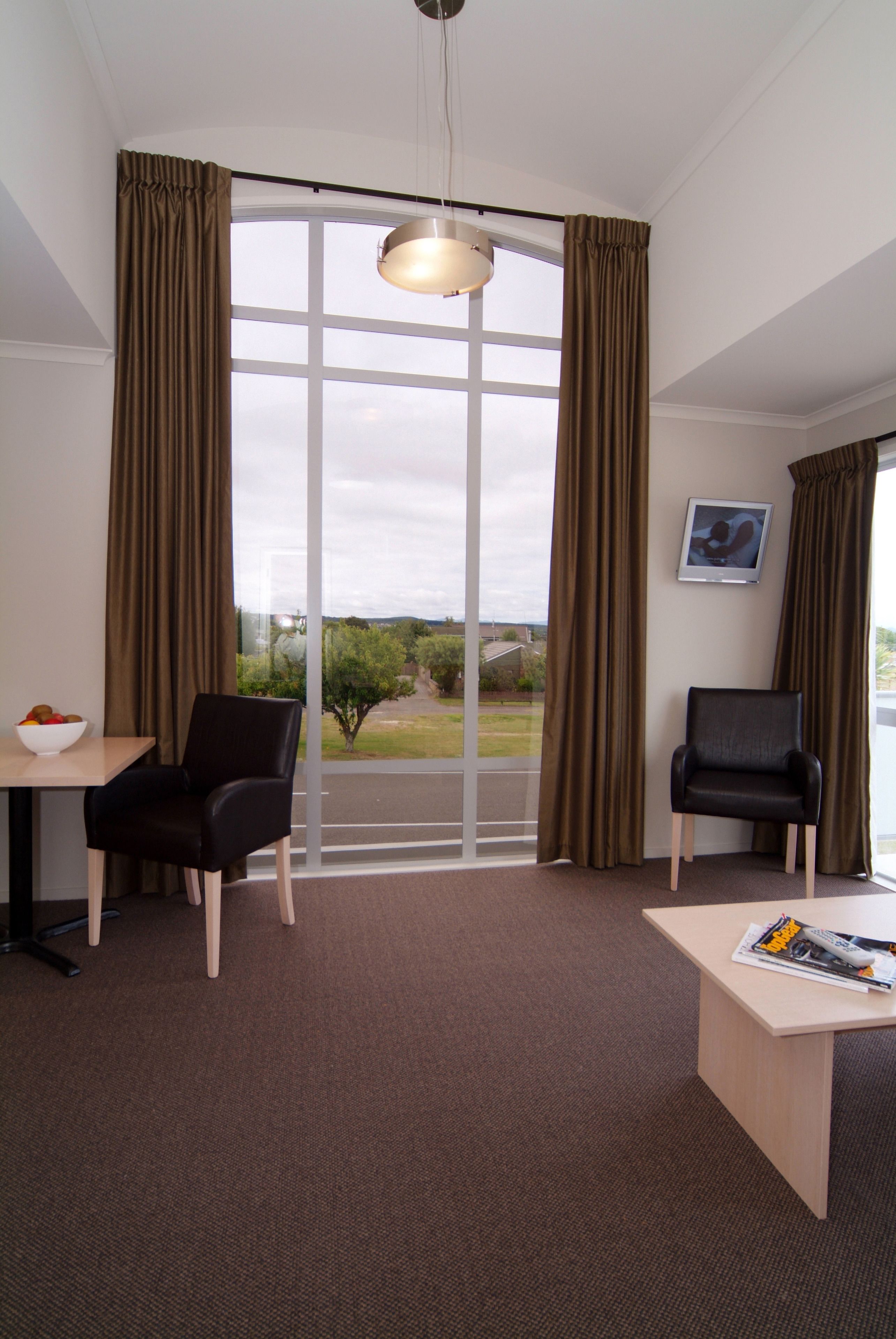 A hotel room with a large window, two chairs, a table, and a bowl of fruit.