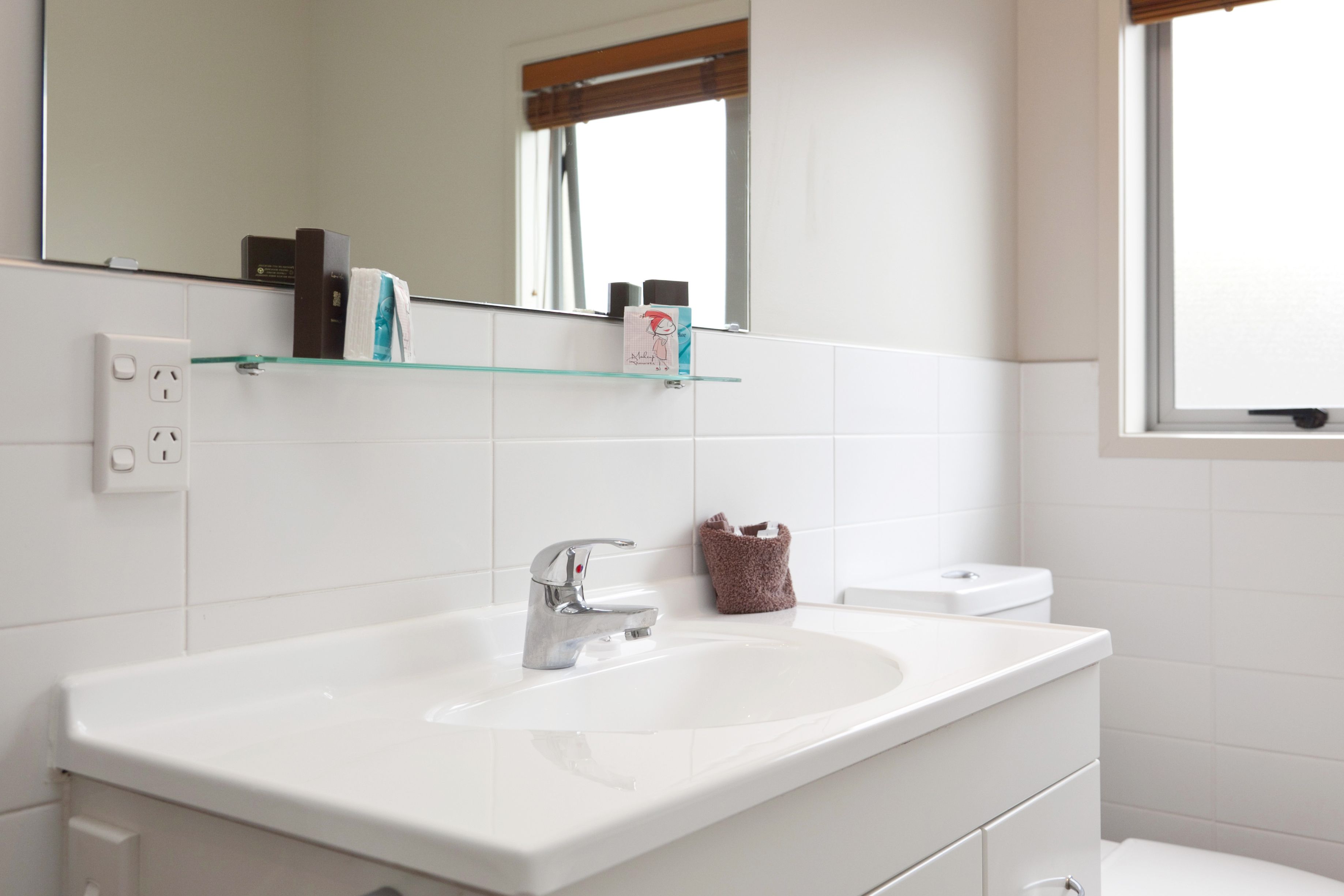 Un baño con lavamanos blanco, un espejo y una ventana.