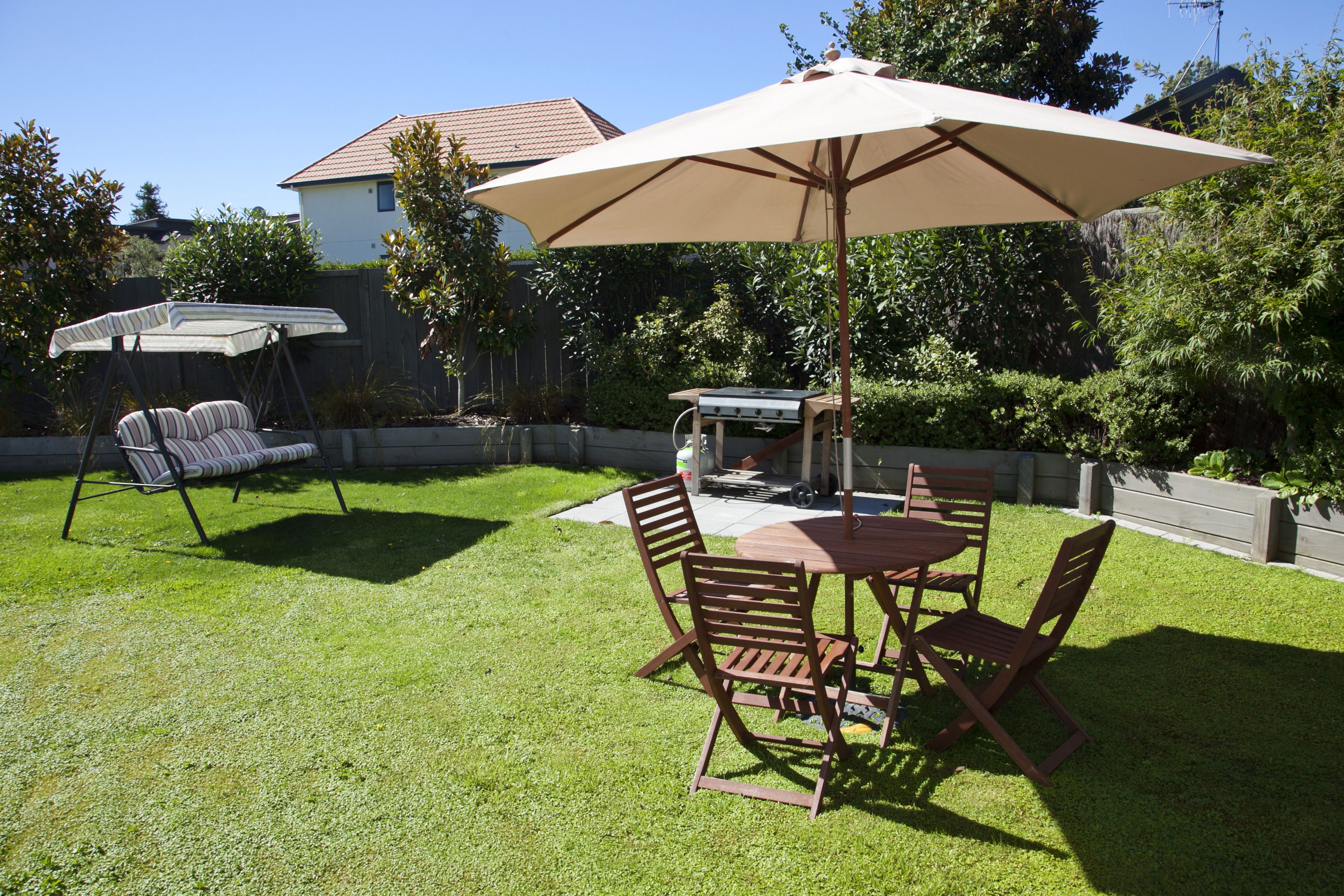 A backyard with a dining table, chairs, and a large umbrella.