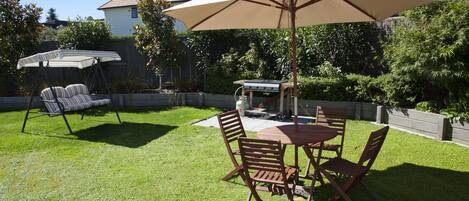 Un patio trasero con mesa, sillas y un gran paraguas.