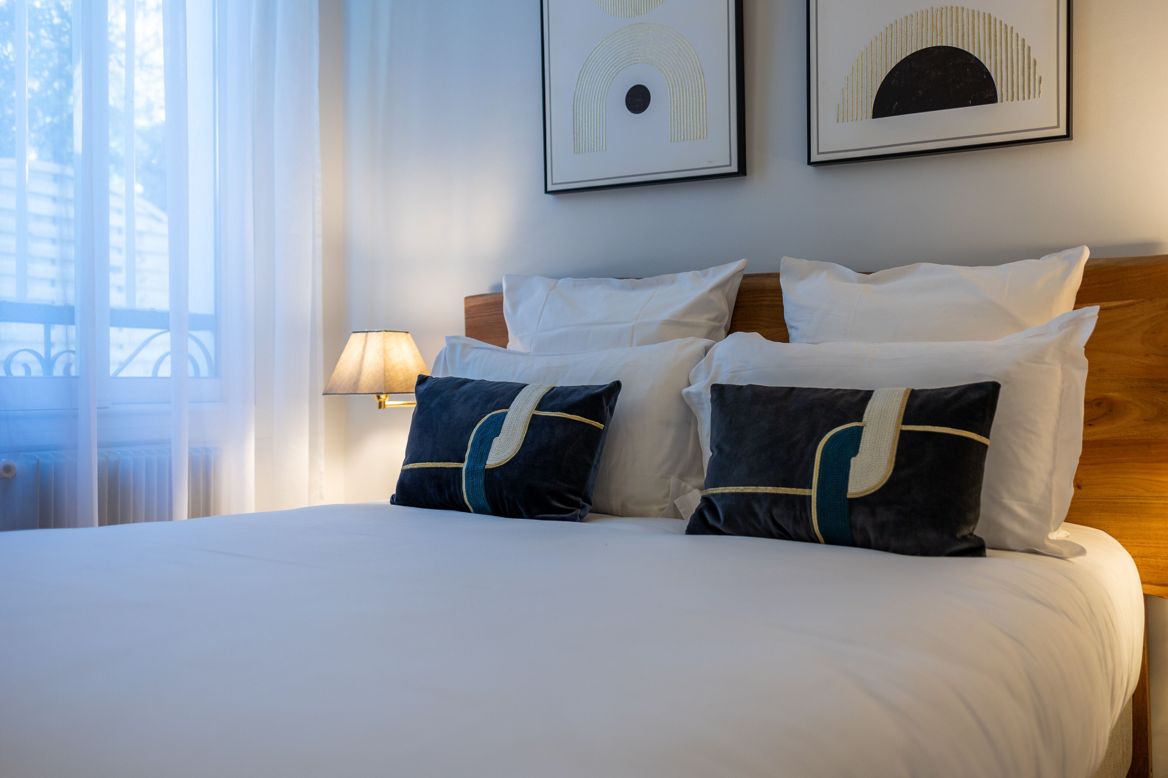 A neatly made bed with white and navy pillows, a wooden headboard, and two framed artworks on the wall.