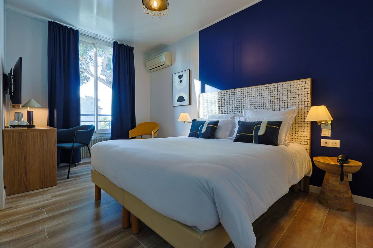 A modern hotel room with a large bed, a desk, a chair, and a view of the outdoors.