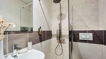 A modern bathroom with a glass shower enclosure, a white sink, and a mirror.