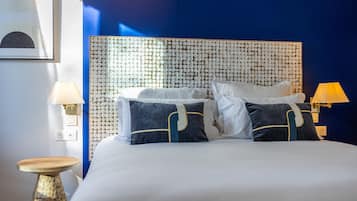 Una cama bien hecha con almohadas blancas y azul oscuro, un cabecero con textura y dos lámparas de noche.