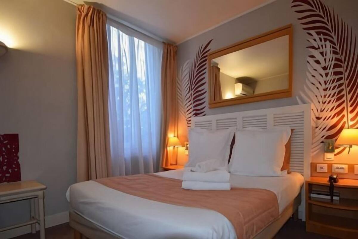 A hotel room with a bed, a nightstand, a mirror, and a window with curtains.