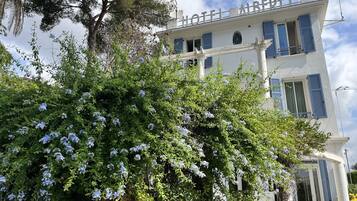 A hotel with a white facade, blue shutters, and a sign reading "HOTEL AIRSTER".