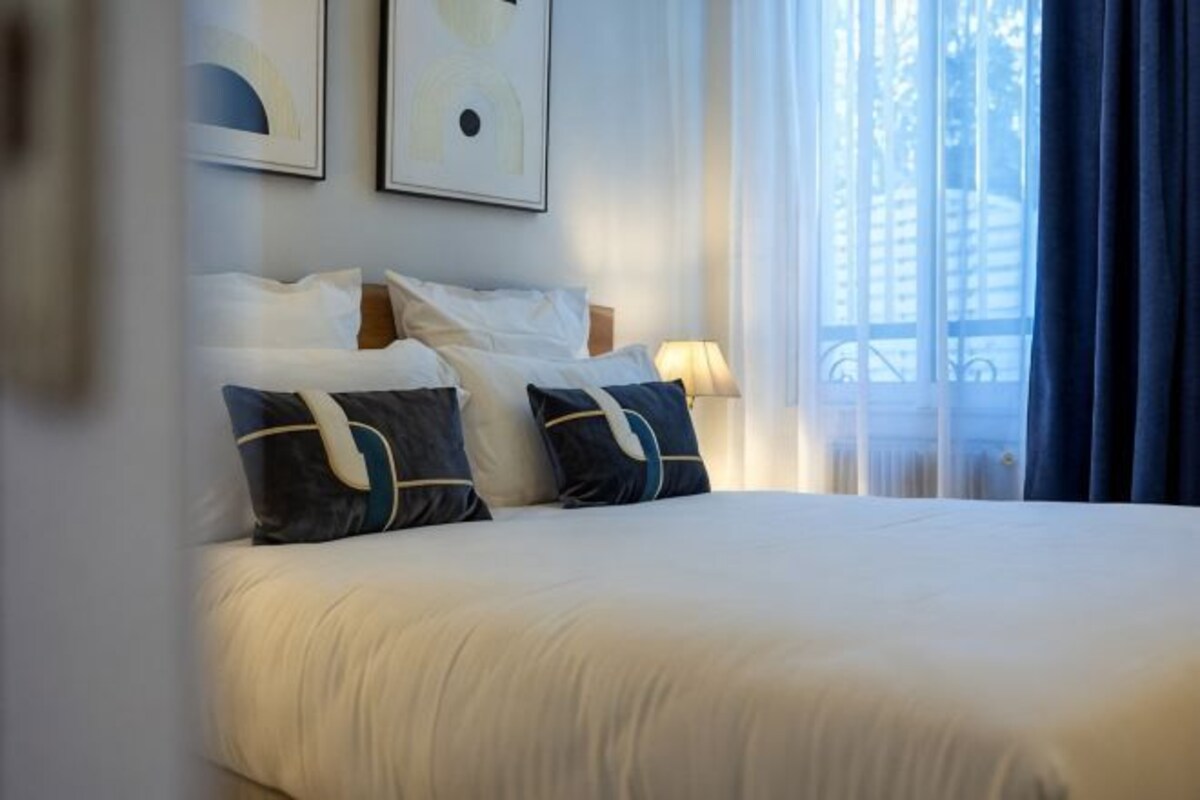 A hotel room with a large bed, a nightstand, and a window with curtains.