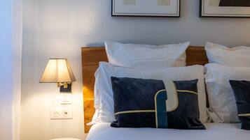 Una cama bien tendida con almohadas blancas y azul oscuro, un cabecero de madera y una lámpara de pared.