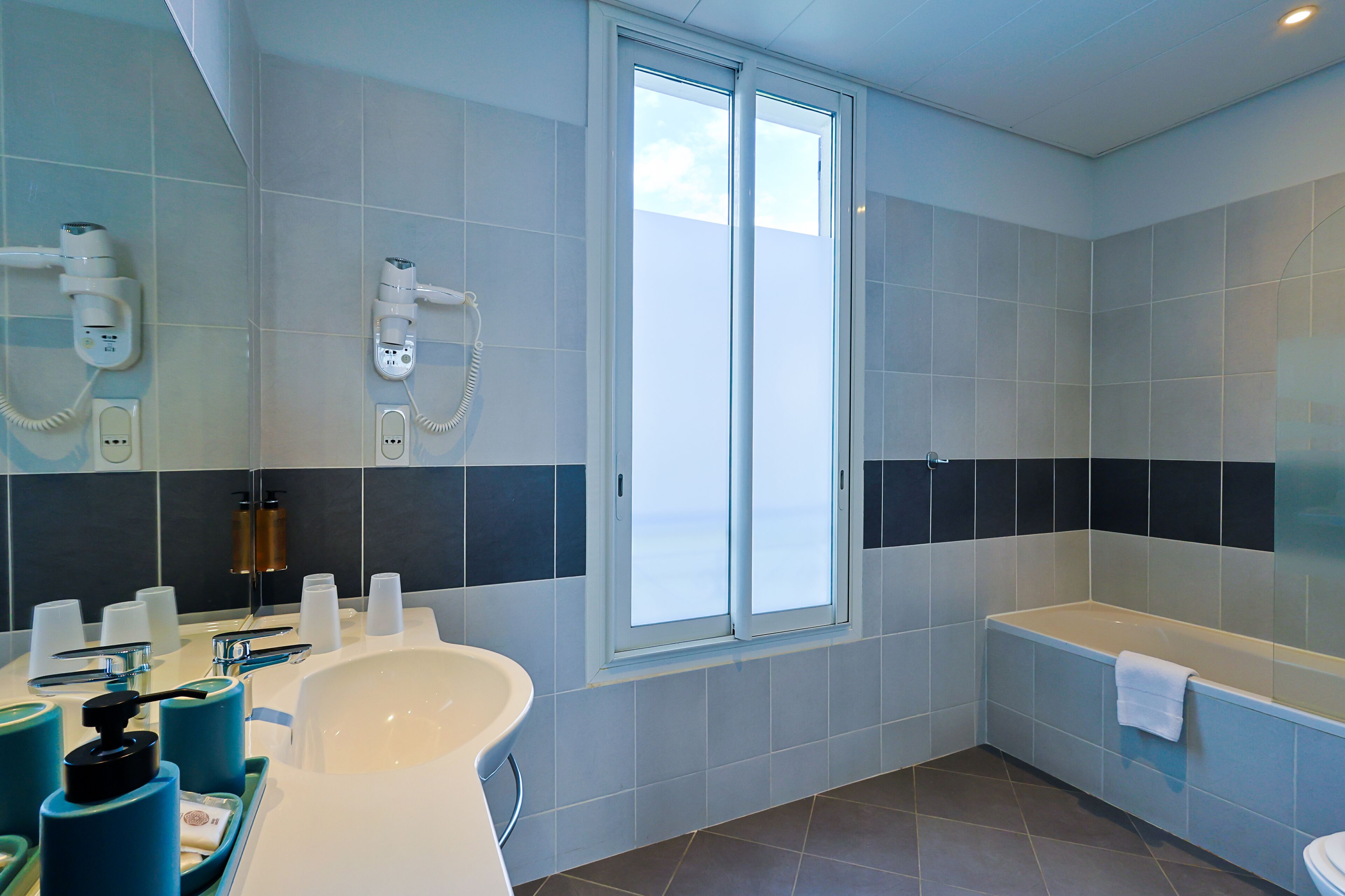 Une salle de bain moderne dotée d’une grande baignoire, d’une douche avec un pommeau réglable et d’une fenêtre laissant entrer la lumière naturelle.