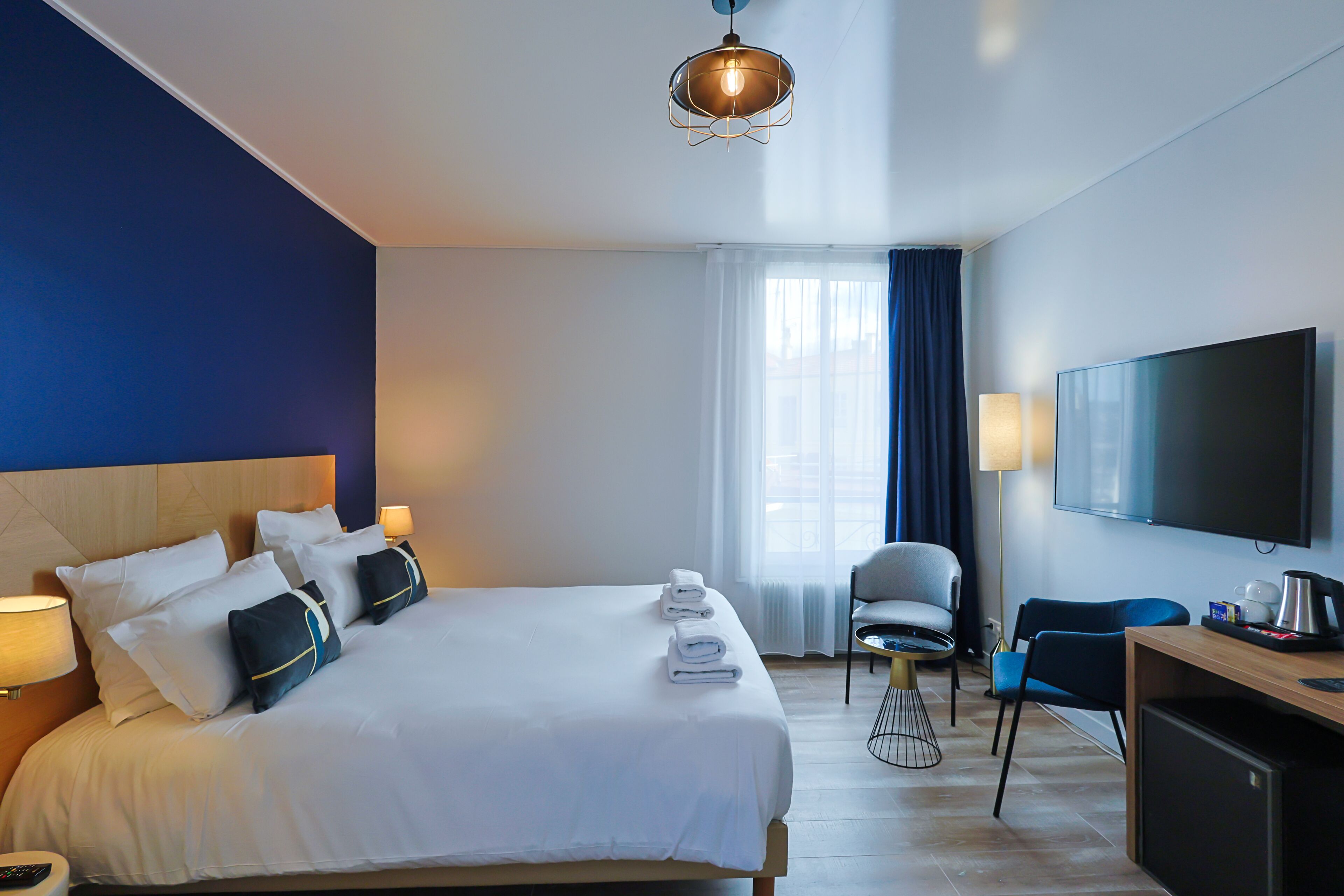 Ett hotellrum med en stor säng, ett skrivbord med en dator, en stol, en tv och ett fönster med gardiner.