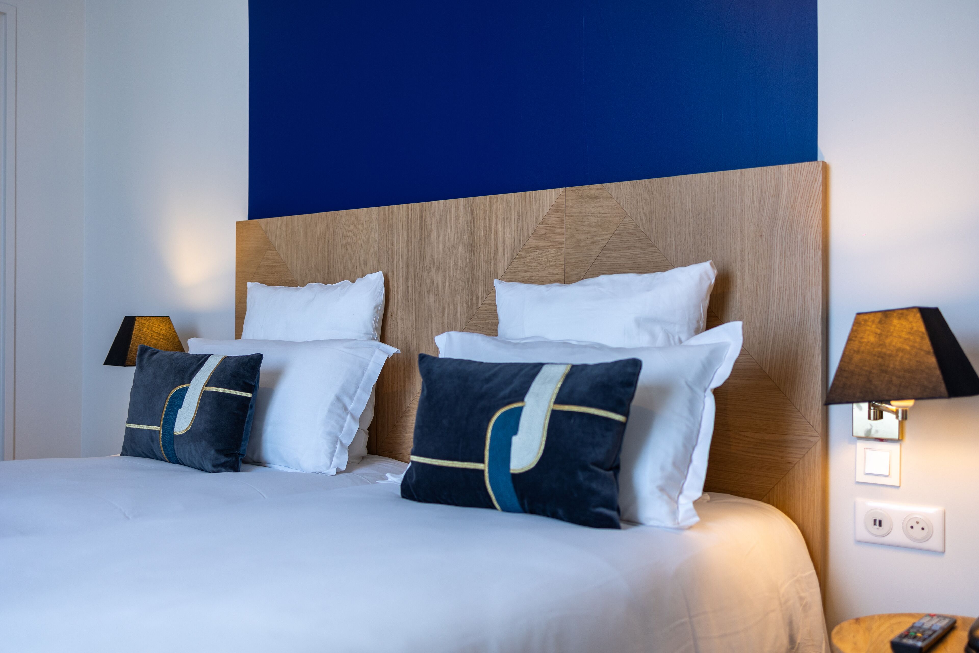 A neatly made bed with white and navy pillows, a wooden headboard, and two bedside lamps.