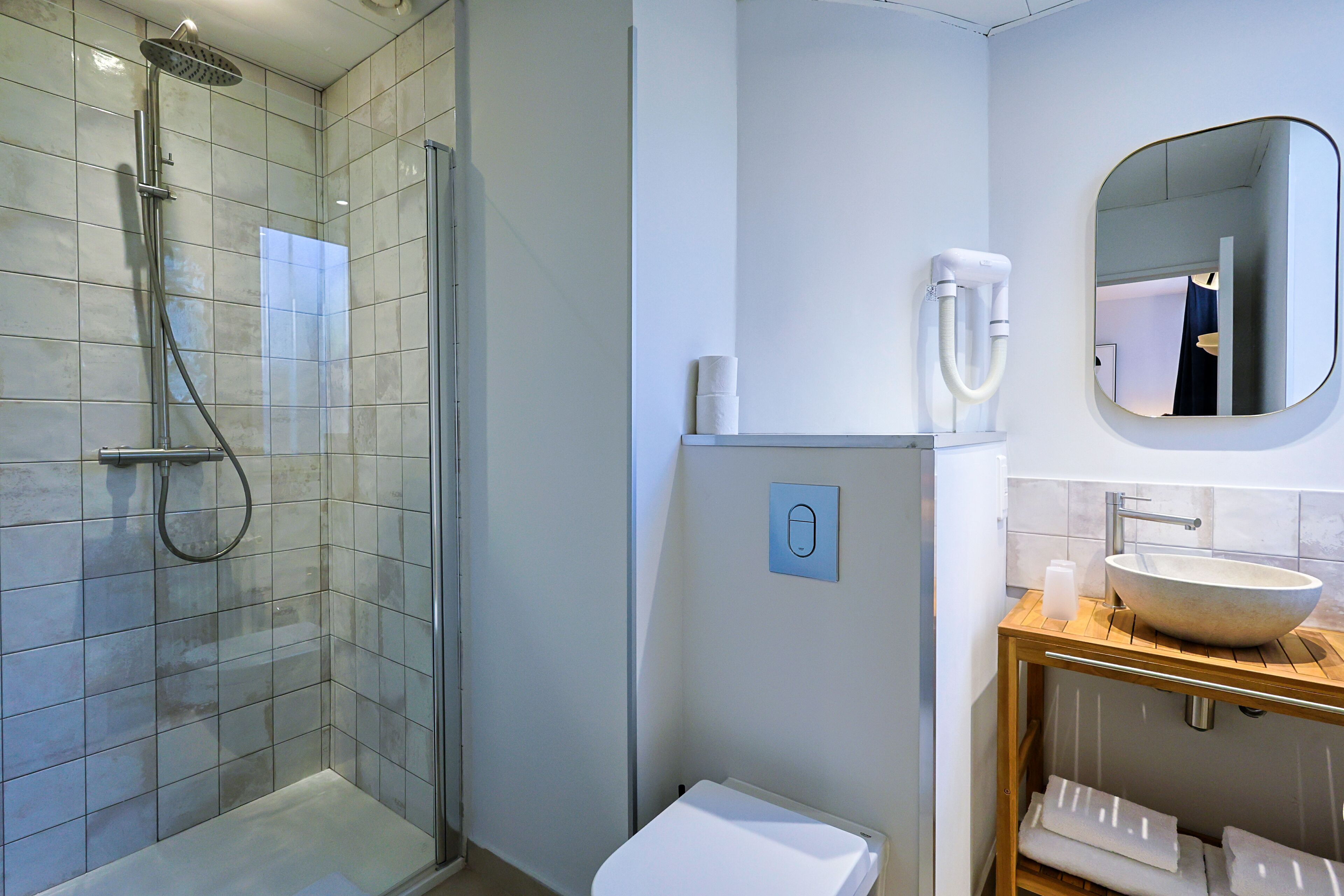 Un baño moderno con ducha de vidrio, inodoro blanco y tocador de madera con un espejo grande.