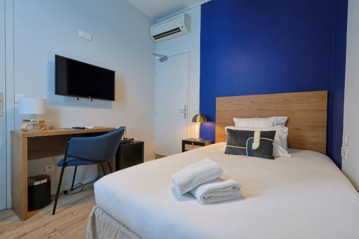 A hotel room with a bed, a desk, a chair, a television, and a nightstand.