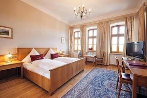 A hotel room with a large bed, a desk, a television, and a chandelier.