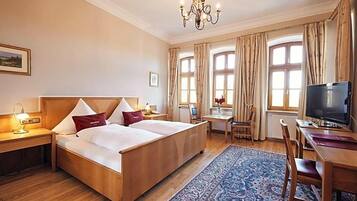 A hotel room with a wooden bed, a desk, a television, and a large window with curtains.