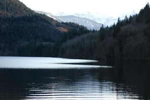 Un lac paisible, entouré d’une forêt dense et dominé, au loin, par des montagnes enneigées.