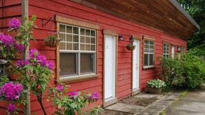 A red wooden house with white-framed windows, a front door, and hanging flower baskets.