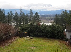 Une cour verdoyante avec un mur de pierre, des arbres et une vue sur des montagnes lointaines.