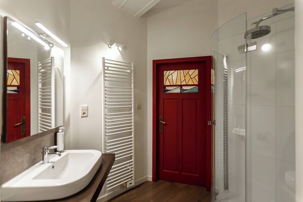 Un baño con un lavabo blanco, una puerta roja y una cabina de ducha de vidrio.