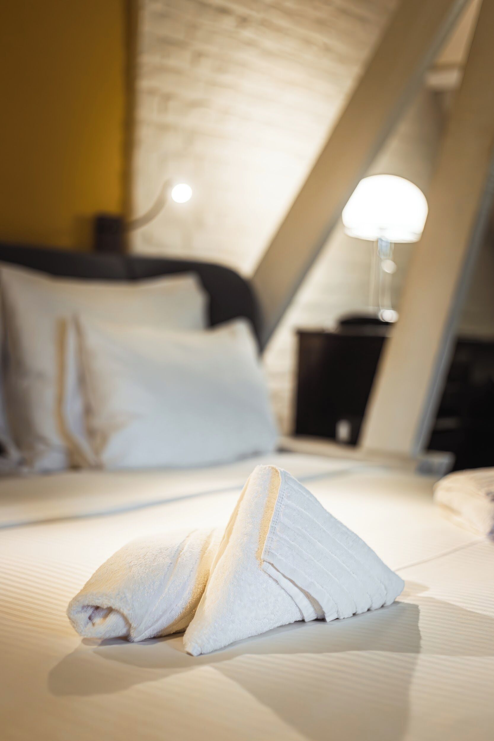 Una cama bien hecha con una toalla doblada al frente, una lámpara de noche y un cabecero en una habitación de hotel.