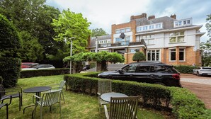 Un edificio residencial con un jardín delantero, un coche negro estacionado adelante y un coche blanco en la entrada.