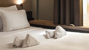 Una cama bien hecha con almohadas y una toalla enrollada, una lámpara de pared y una ventana con cortinas.