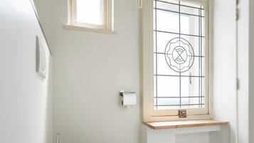 Un baño con inodoro, una ventana con celosía decorativa y un estante de madera.
