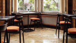 Un restaurante con una zona de asientos en esquina, amplias ventanas con vistas a árboles y edificios, y un piso de madera pulida.