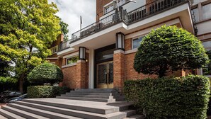 Un edificio residencial de varios pisos con fachada de ladrillo, un balcón con barandilla de metal y una escalera de piedra que conduce a la entrada.