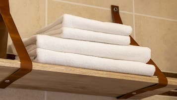 Une pile de serviettes blanches est posée sur une étagère en bois, soutenue par des équerres en métal.