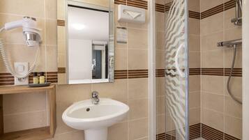 Baño con lavamanos, espejo, dispensador de toallas y ducha.