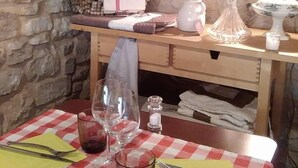 A rustic kitchen with stone walls, a wooden table set for dining, and various kitchen utensils and appliances. - Hôtel Le Crillon (Murs)