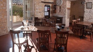 A rustic dining area with stone walls, wooden tables and chairs, and a clock on the wall. - Hôtel Le Crillon (Murs)