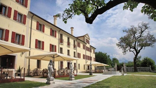 A building with multiple balconies, outdoor seating areas, and a statue in the courtyard. - Villa Carpenada (Belluno)