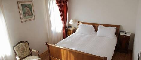 A bedroom with a wooden bed, a chair, a nightstand, a lamp, and a painting on the wall.