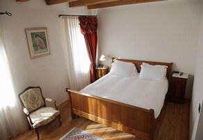 Un dormitorio con una cama de madera, una silla, una mesita de noche, una lámpara y un cuadro en la pared.
