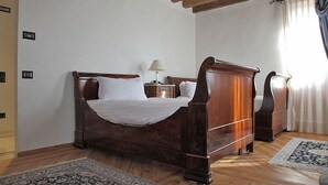 A wooden bed with white linens in a room with wooden floors and a ceiling with exposed beams. - Villa Carpenada (Belluno)