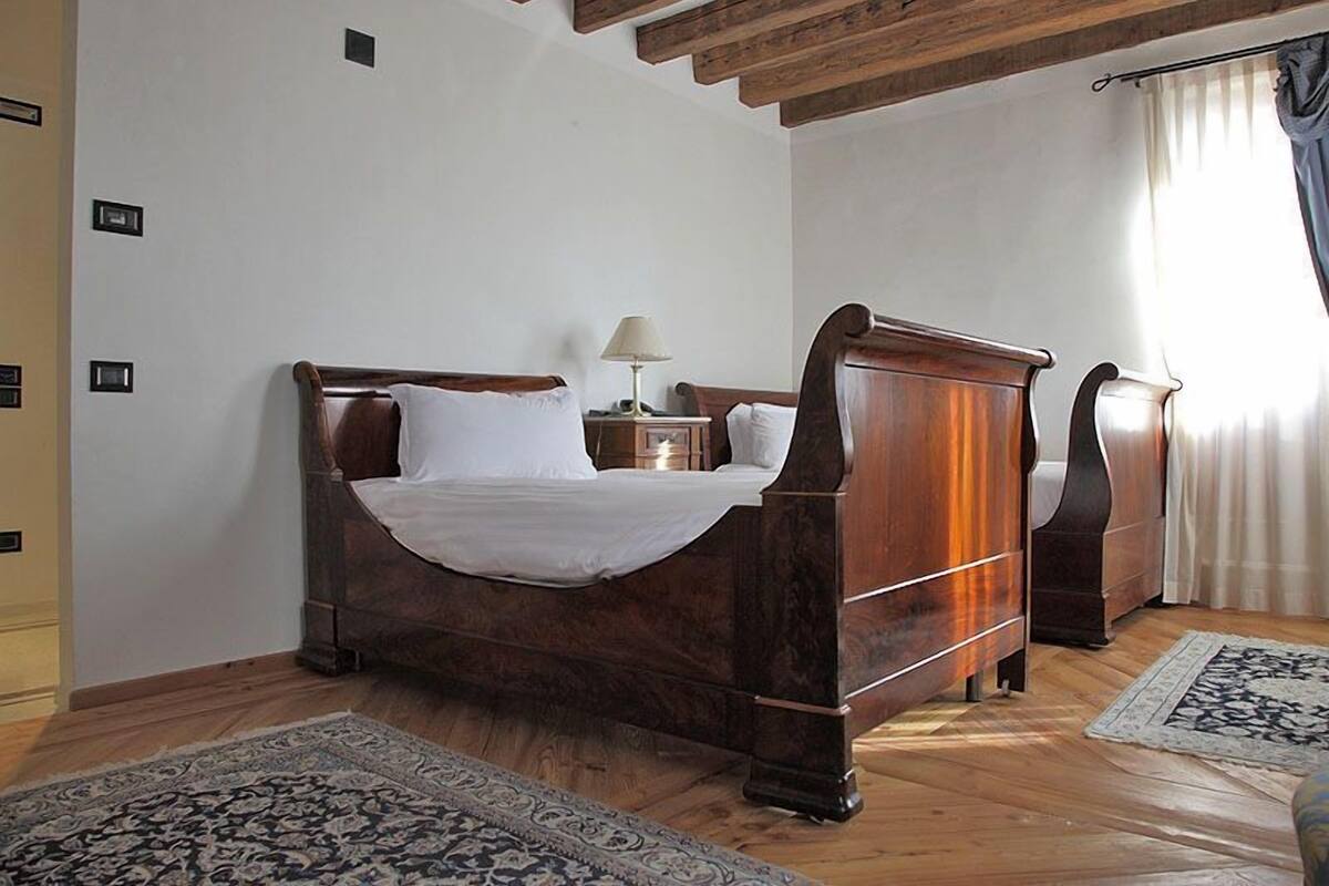 A wooden bed with white linens in a room with wooden floors and a ceiling with exposed beams.