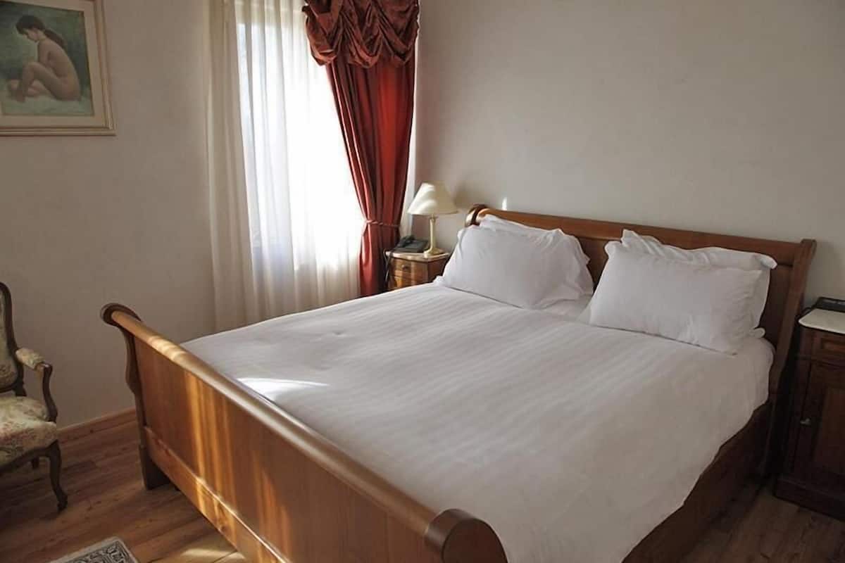A neatly made bed with white linens, a wooden headboard, and a nightstand with a lamp.