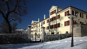A large, multi-story building with red shutters, a stone wall, and a snow-covered ground. - Villa Carpenada (Belluno)