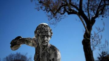 Una estatua de una figura con los brazos extendidos, frente a un cielo azul despejado y un árbol.