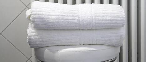 A white bathroom with a white towel stacked on a white toilet seat.