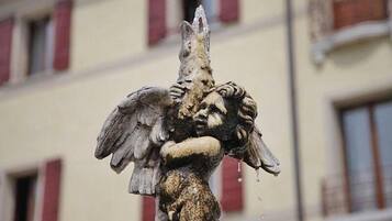 A weathered statue of a winged creature holding a human head, set against a building with red window frames.