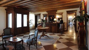 A lobby with checkered flooring, wooden furniture, a reception desk, and a large vase with flowers. - Villa Carpenada (Belluno)