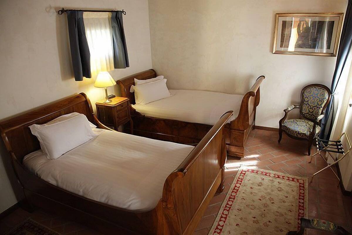 A room with two wooden beds, a small table with a lamp, a patterned rug, and a chair.