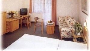 Una habitación de hotel con una cama, un escritorio con televisor, un sofá floral y una pequeña mesa con una planta.